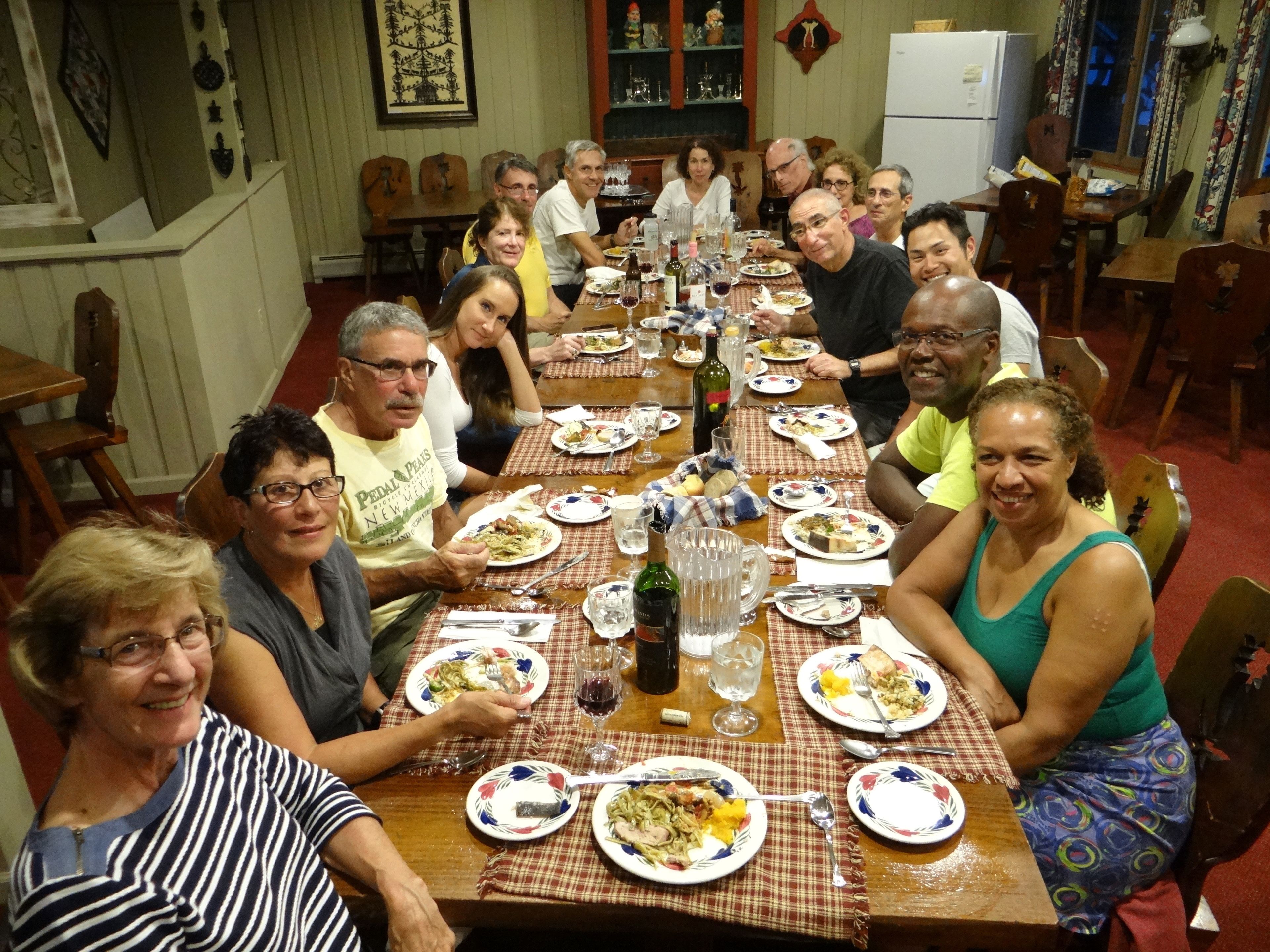 A group of people seated around a long dining table in a room with wooden furniture and a checkered tablecloth.