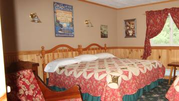 A bedroom with a wooden bed, floral-patterned chairs, a quilt, a poster on the wall, and a window with curtains.