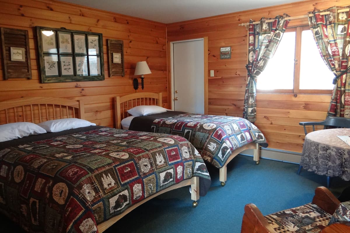 A wooden cabin room with two beds, a table, and a window with curtains.
