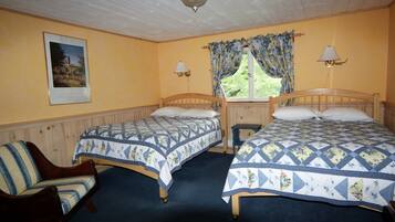 A room with two wooden beds, a chair, a window with curtains, a wall-mounted lamp, and a framed picture.