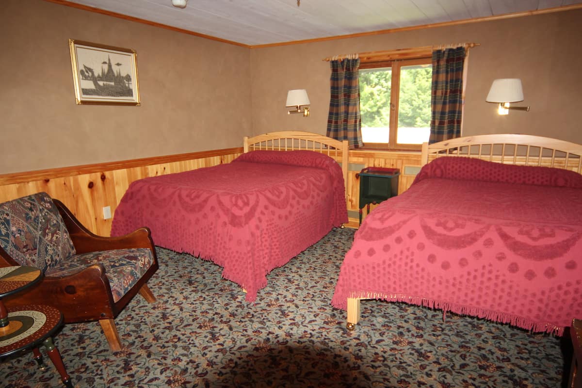 A room with two beds, a wooden chair, a small table, and a window with curtains.
