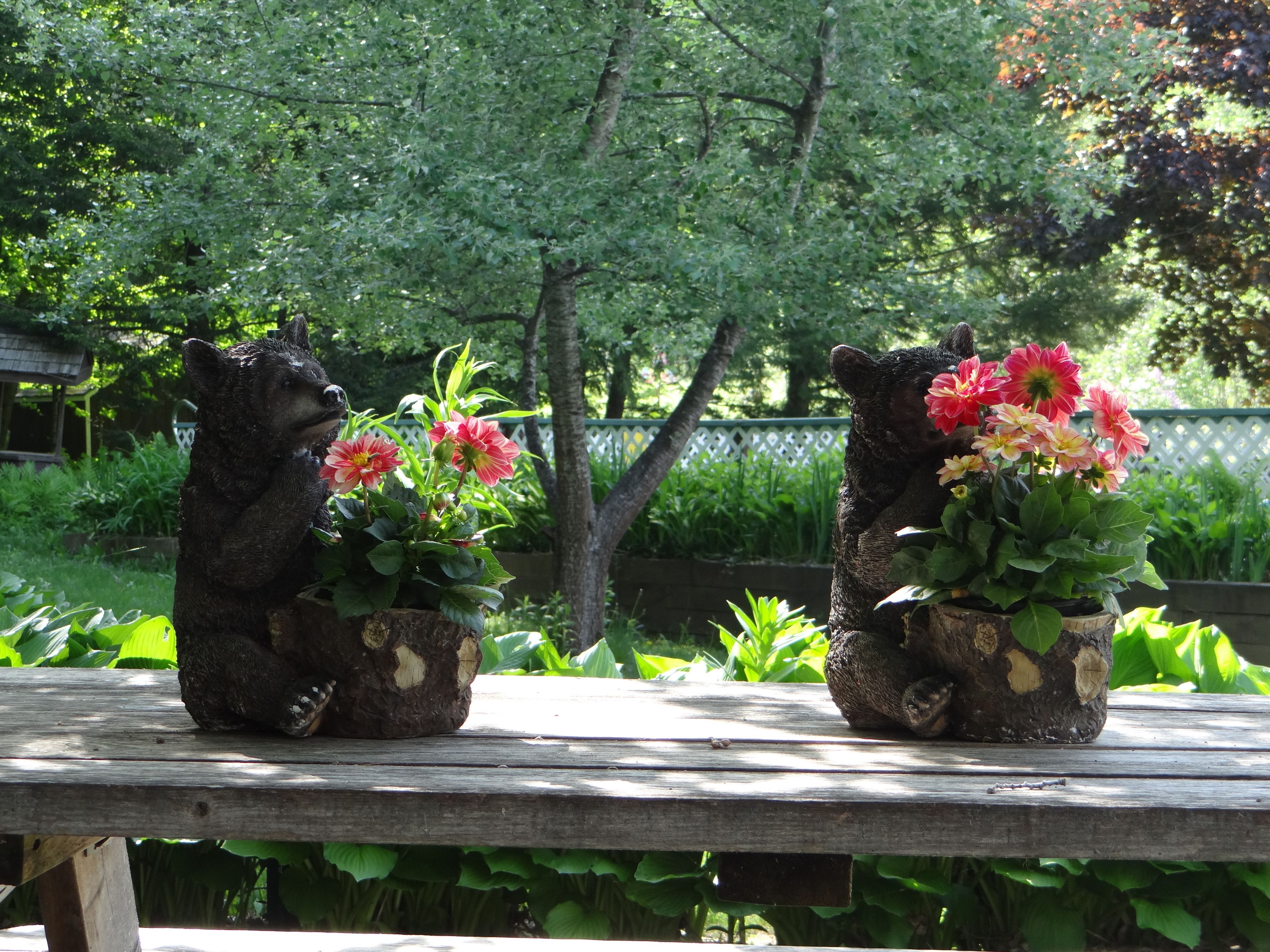 Due fioriere a forma d'orso con fiori su una panchina di legno in un giardino.