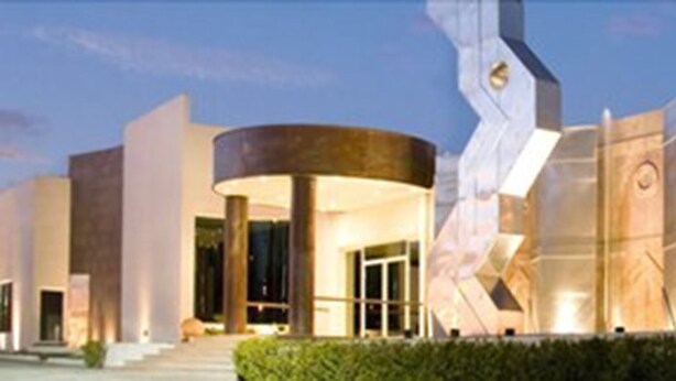 A modern building with a curved entrance, large glass windows, and a prominent sculpture. - Hotel Posada Señorial (San Andrés Cholula)