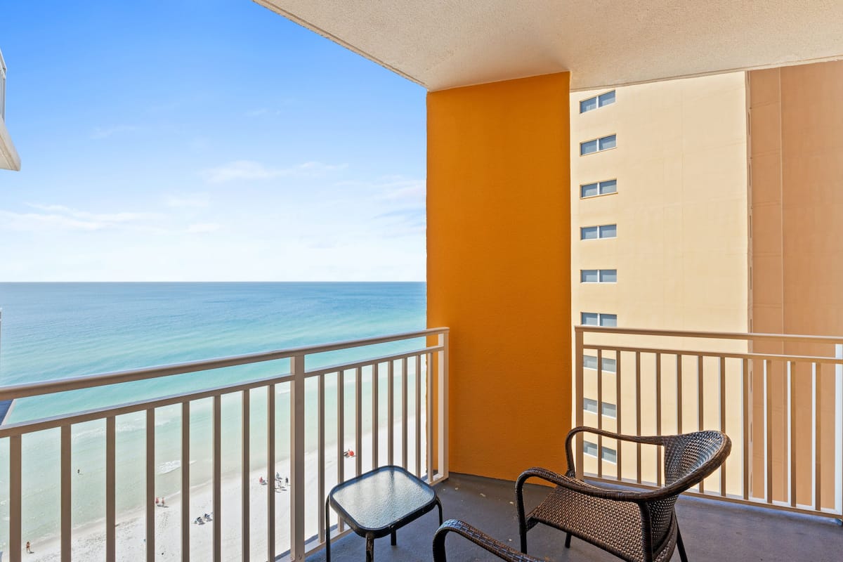 A balcony with a view of the ocean, two wicker chairs, and a small table.