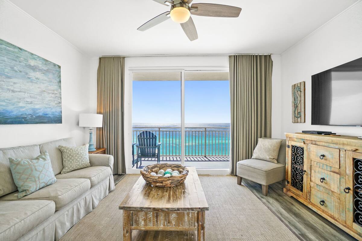 A room with a balcony, a wooden table with a basket, a sofa, a TV, and a cabinet.