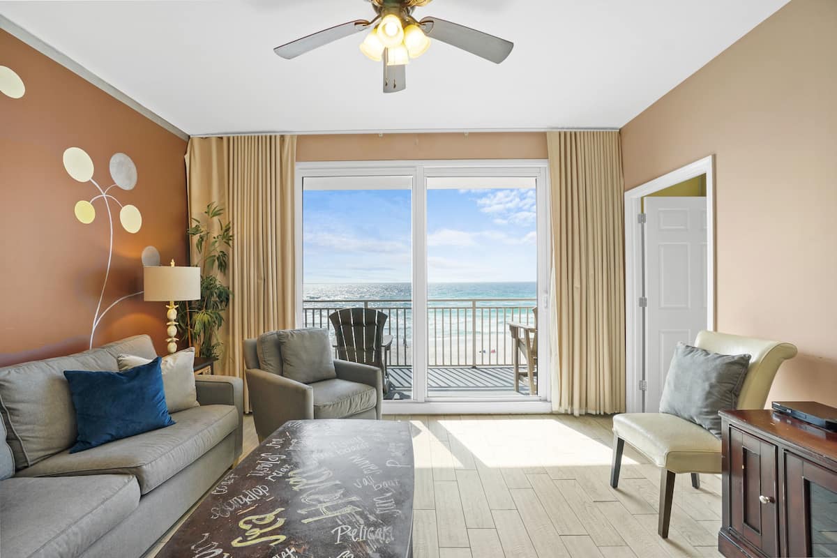 A hotel room with a balcony, a sofa, a chair, a desk, and a ceiling fan.