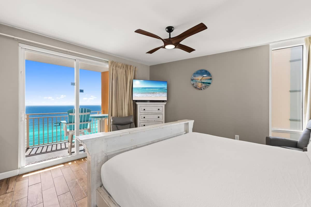 A hotel room with a balcony, a bed, a TV, a dresser, and a ceiling fan.