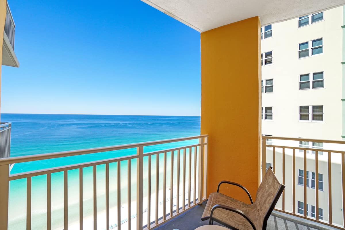 A balcony with a view of the ocean, a chair, and a building with multiple windows.
