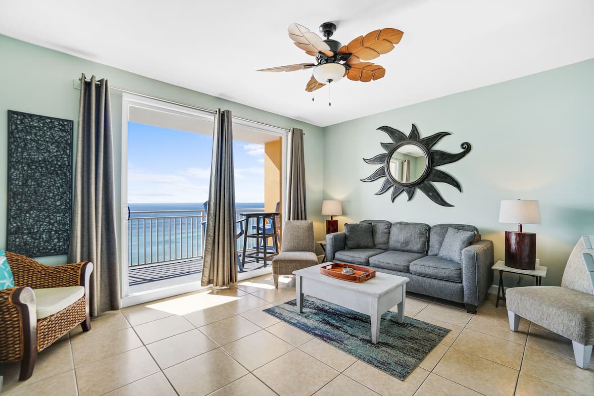 A living room with a balcony, a ceiling fan, a sofa, a coffee table, and a decorative mirror.