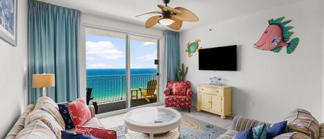 A living room with a view of the ocean, a ceiling fan, a flat-screen TV, and striped sofas.