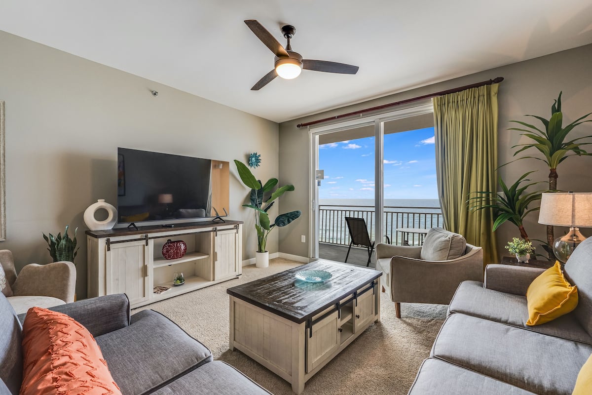 A living room with a TV, sofa, coffee table, and a balcony with a view.