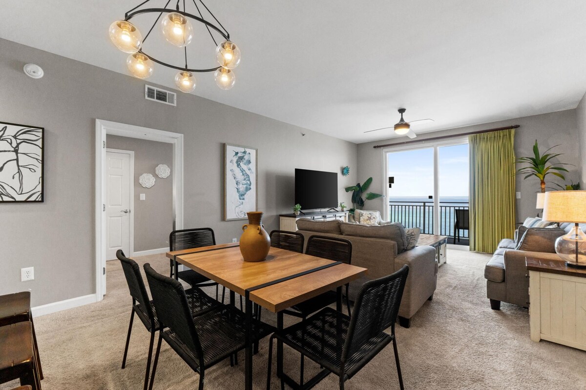 A modern living room with a dining area, a flat-screen TV, and a balcony with a view.