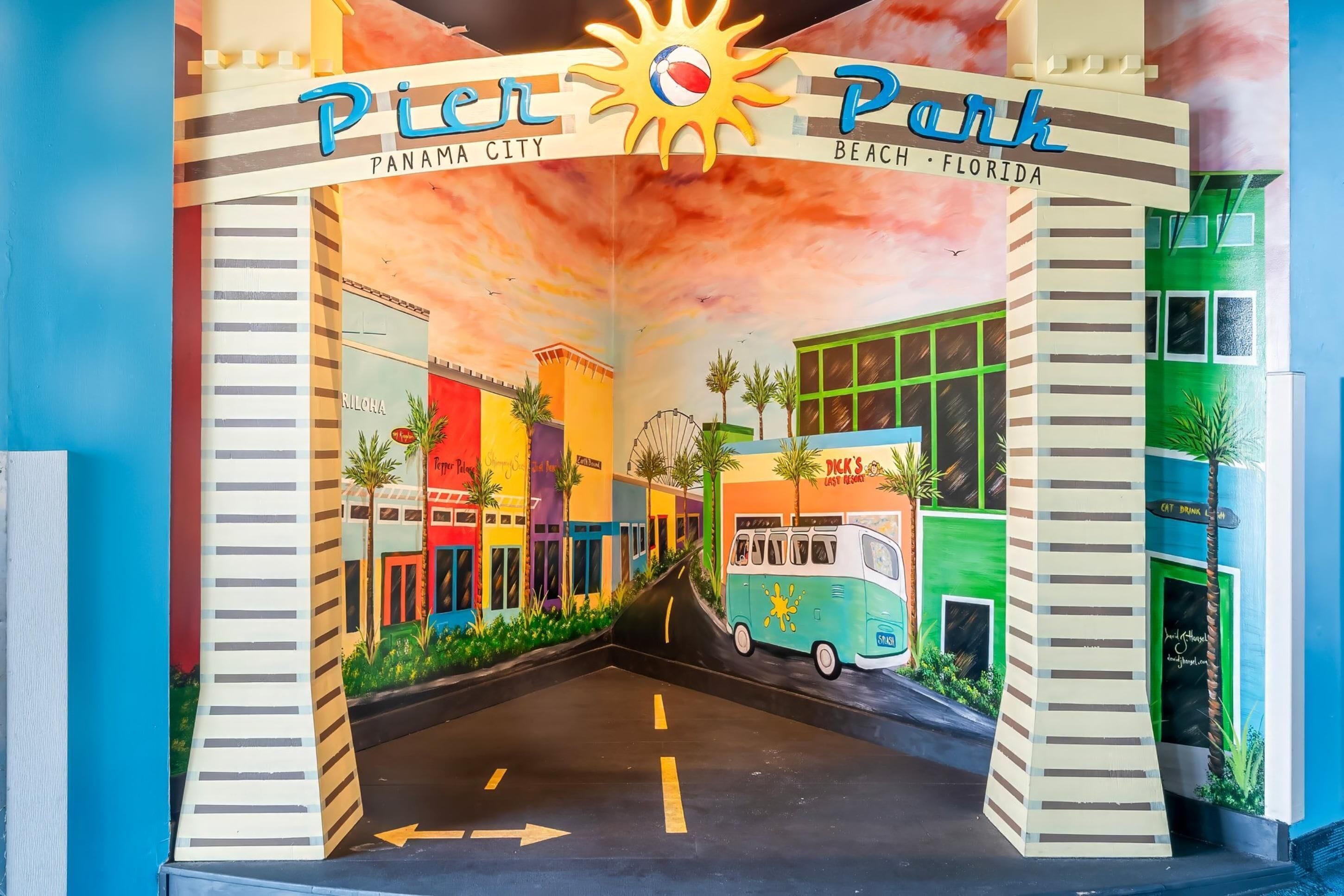 A colorful mural of Pier Park in Panama City, Florida, featuring a van, palm trees, and buildings.
