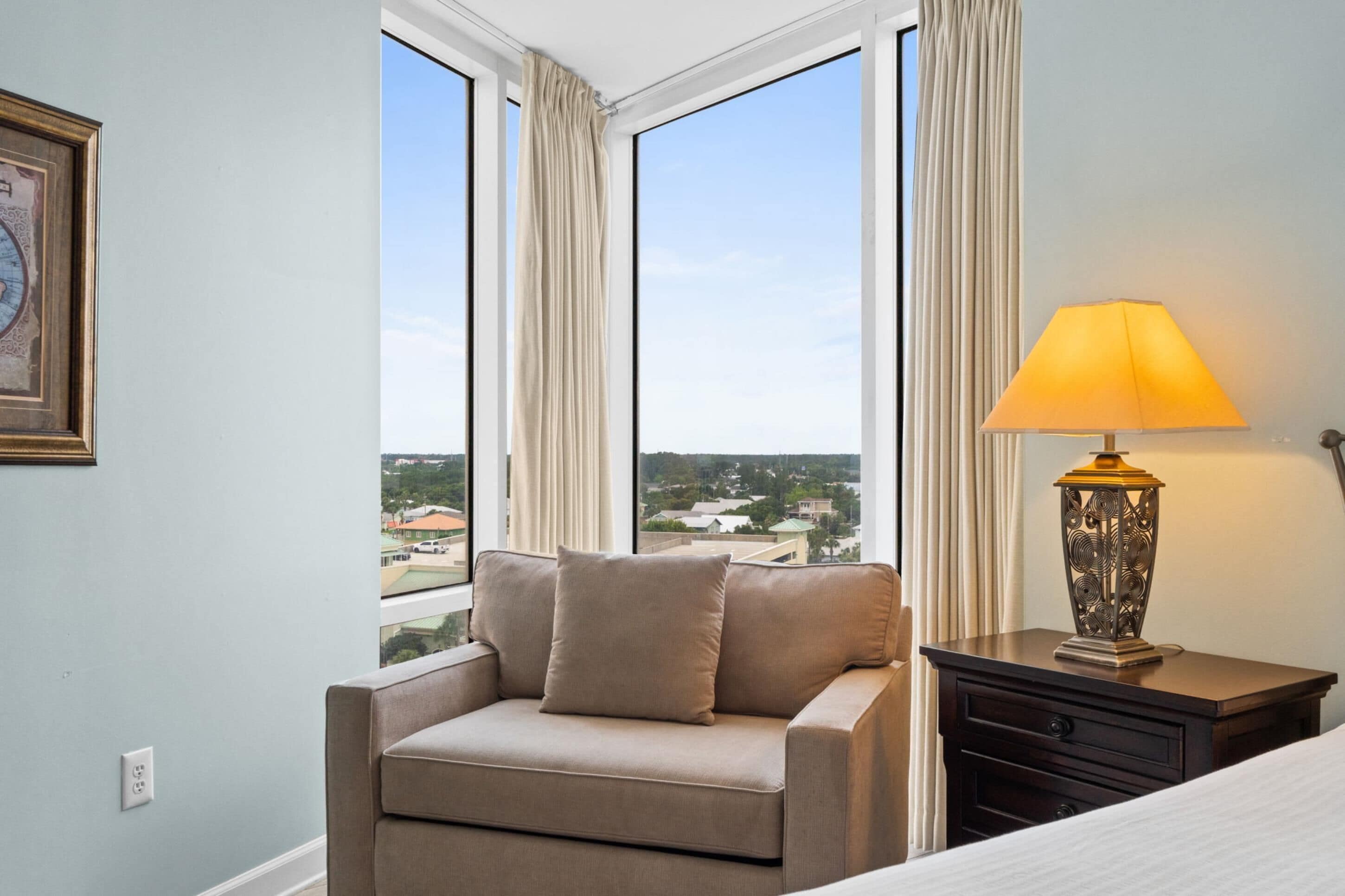 Una habitación con sofá, lámpara y vistas a un paisaje urbano a través de amplios ventanales.