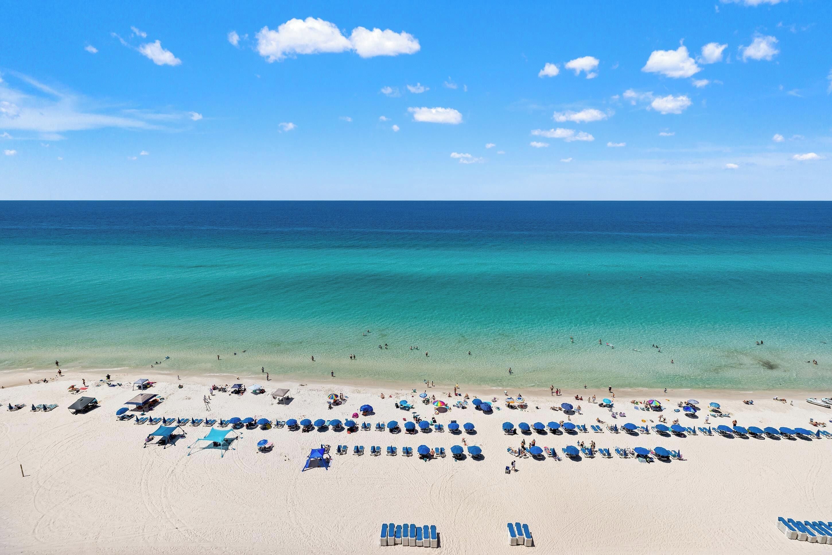 A beach with rows of sun loungers and umbrellas, a clear blue sky, and the ocean.
