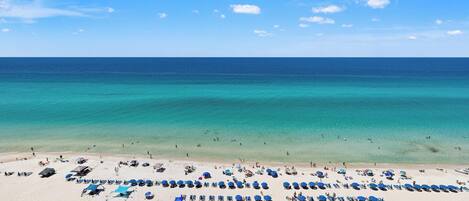 A beach with rows of sun loungers and umbrellas, a clear blue sky, and the ocean.