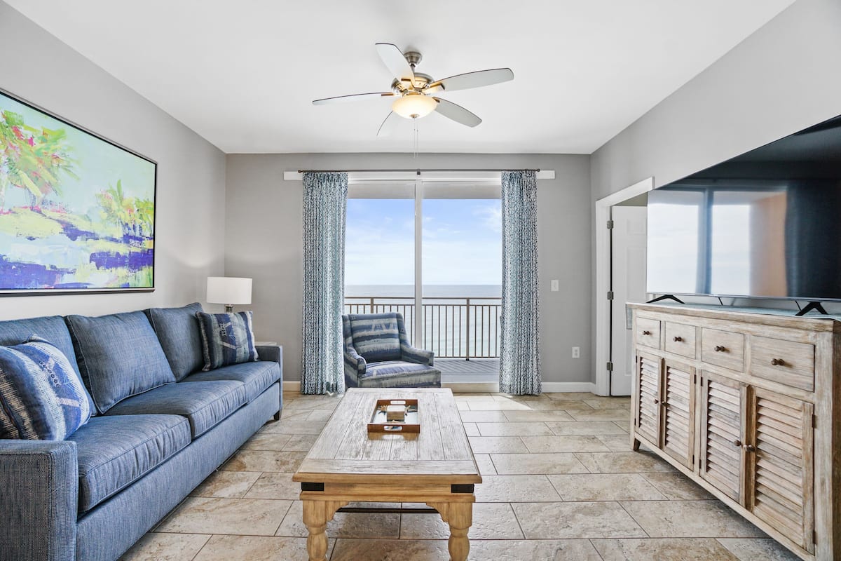 A living room with a sofa, coffee table, TV, and balcony with curtains.