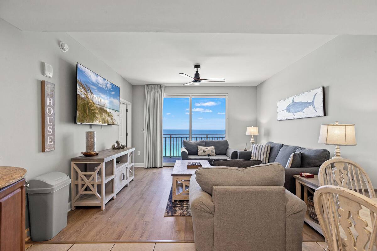 A living room with a TV, sofa, and a view of the ocean.