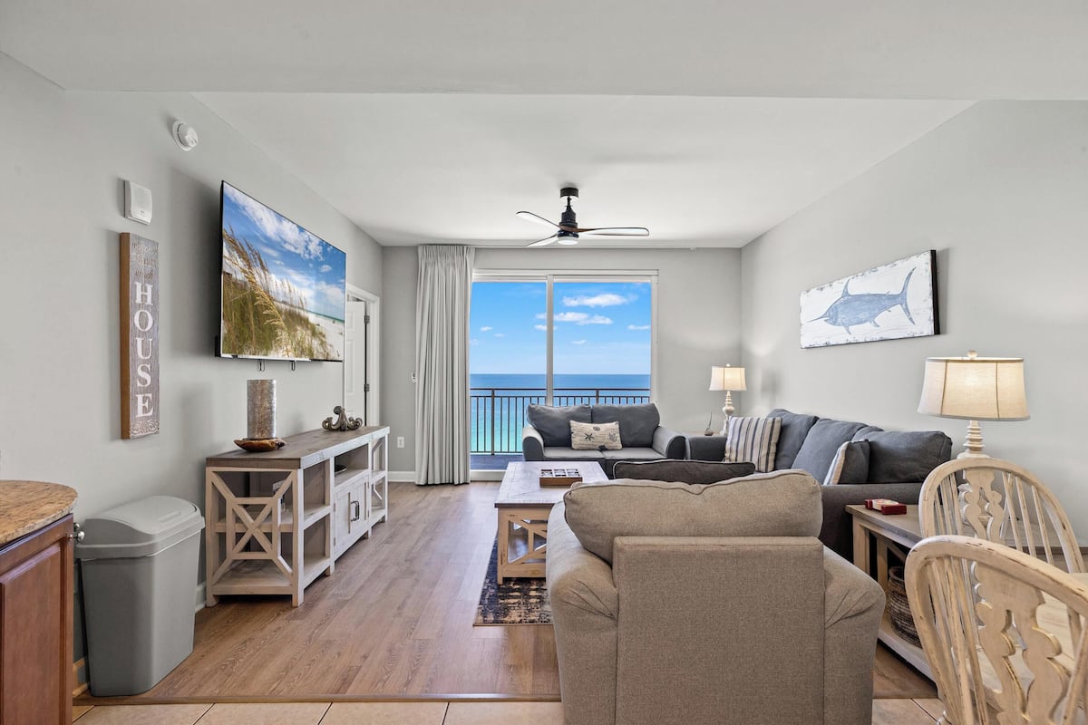 A living room with a sofa, TV, and a view of the ocean.