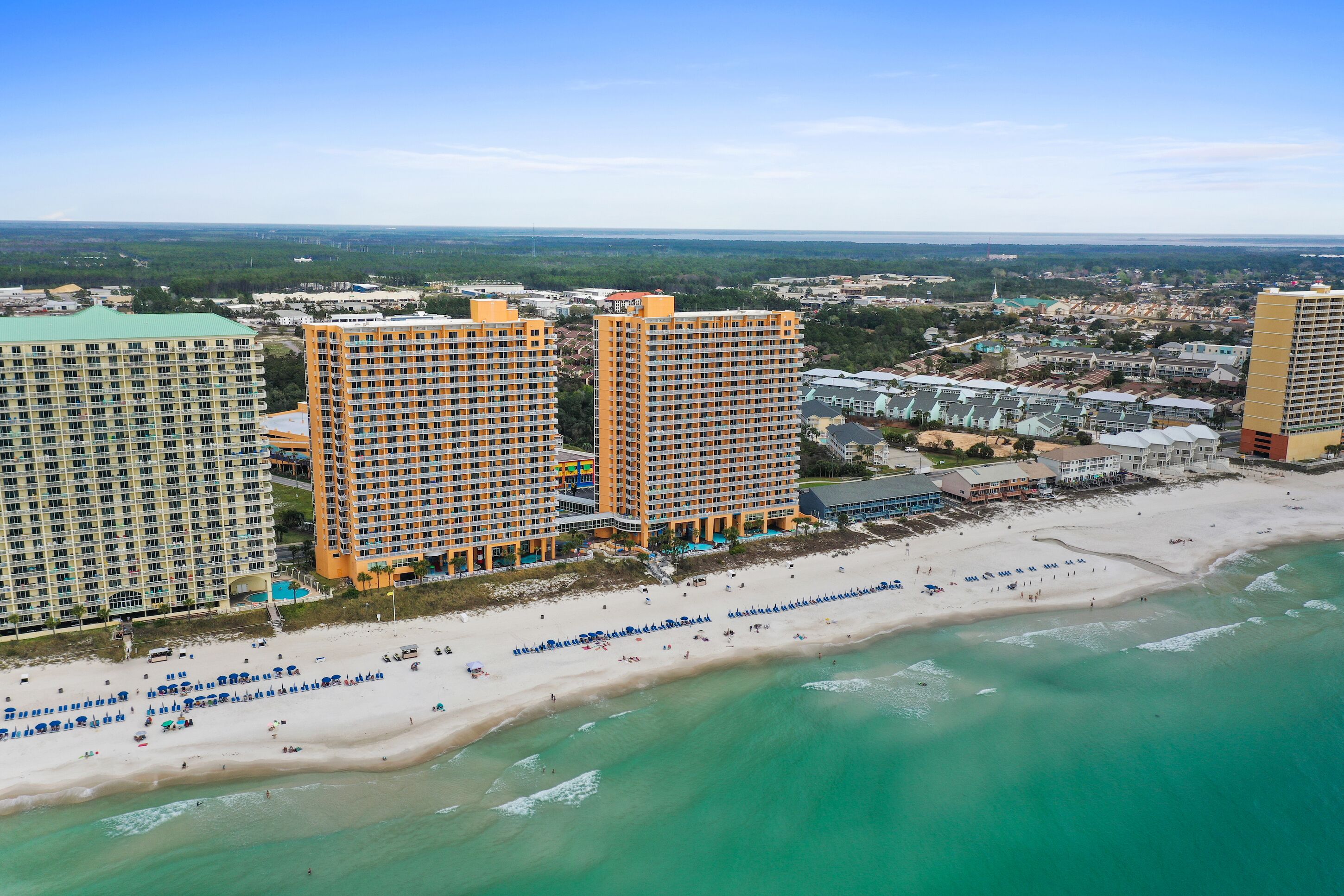 A beachfront hotel with multiple high-rise buildings, a sandy beach, and a clear view of the ocean.