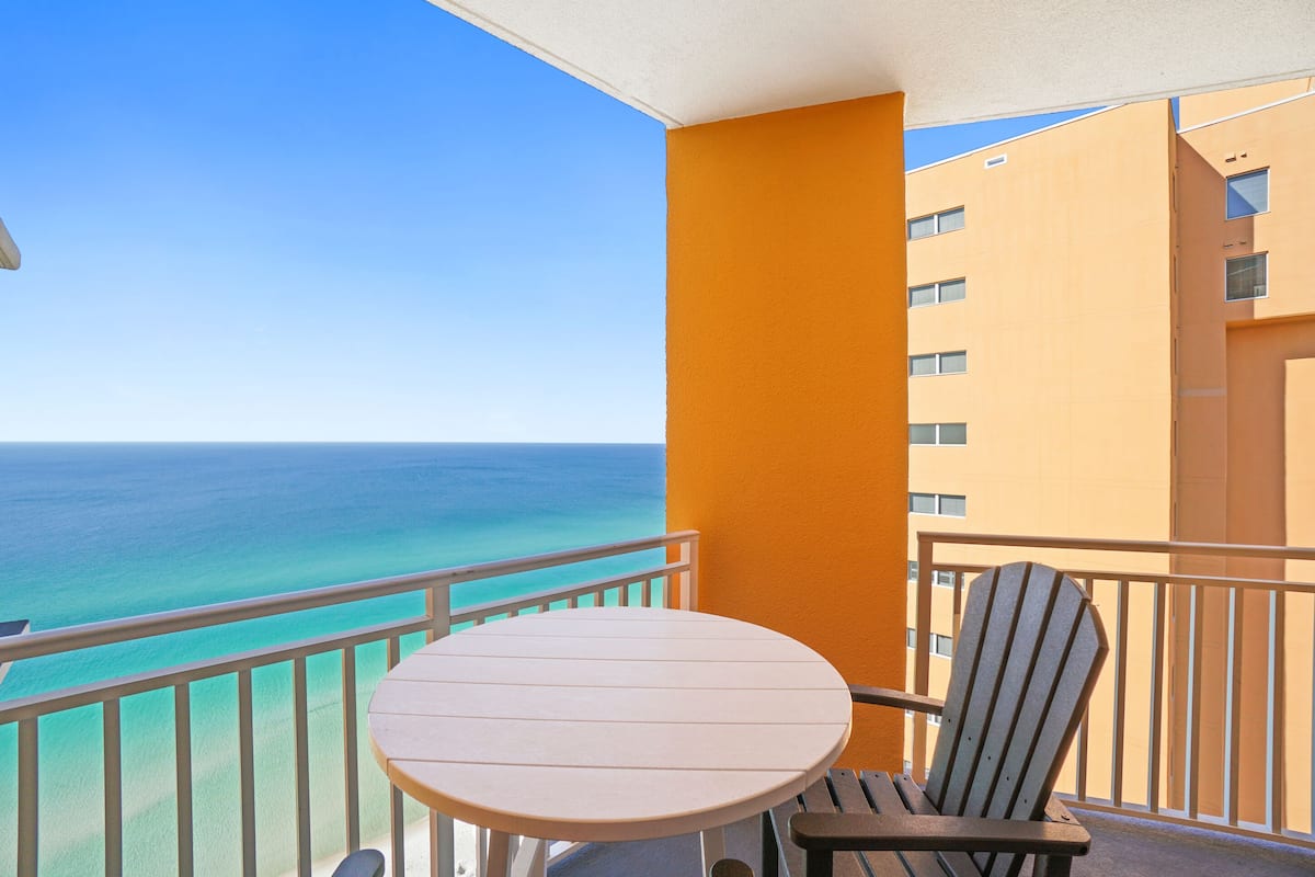 A balcony with a view of the ocean, a round table, and a striped chair.