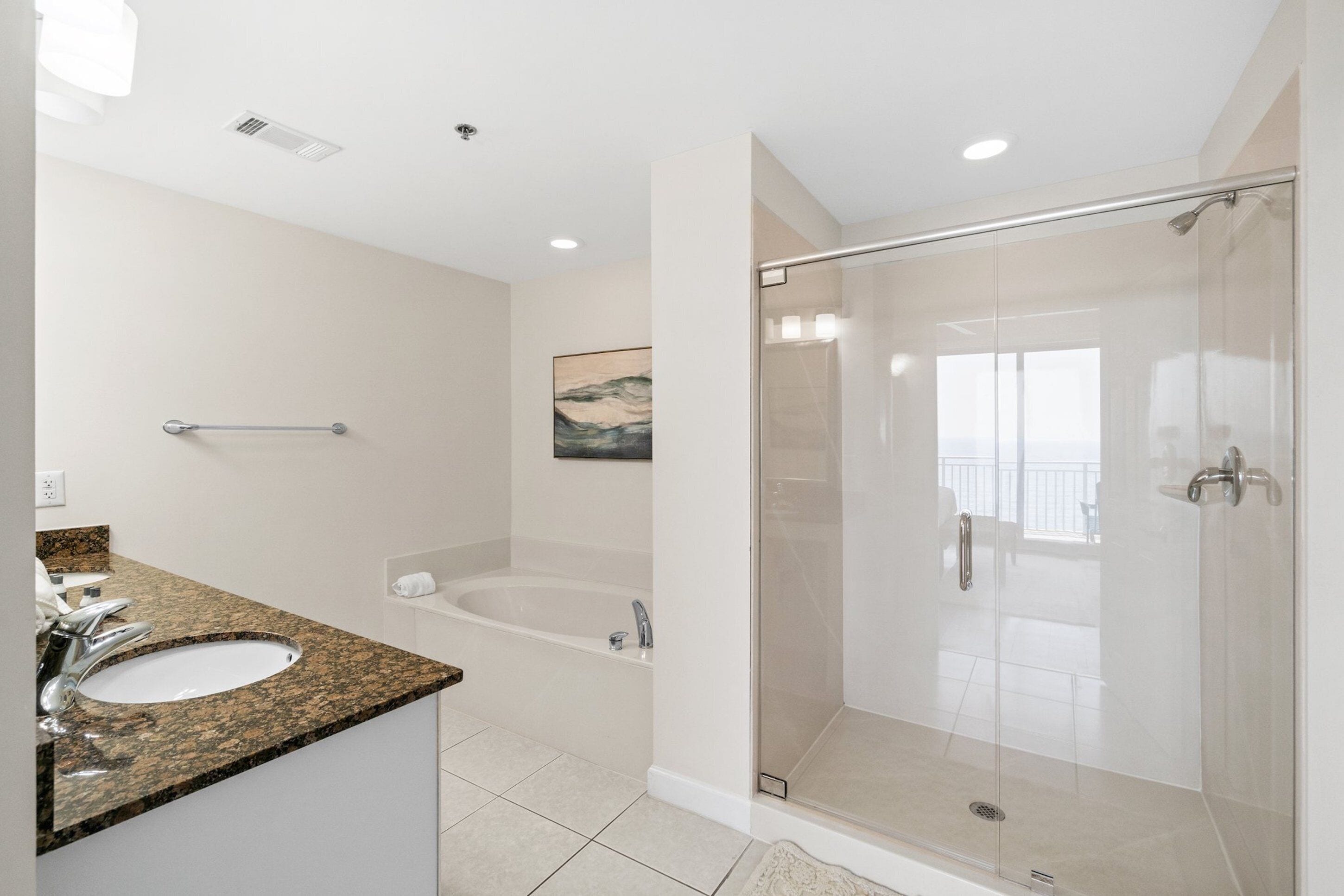 A modern bathroom with a granite countertop sink, a standalone bathtub, and a glass-enclosed shower.