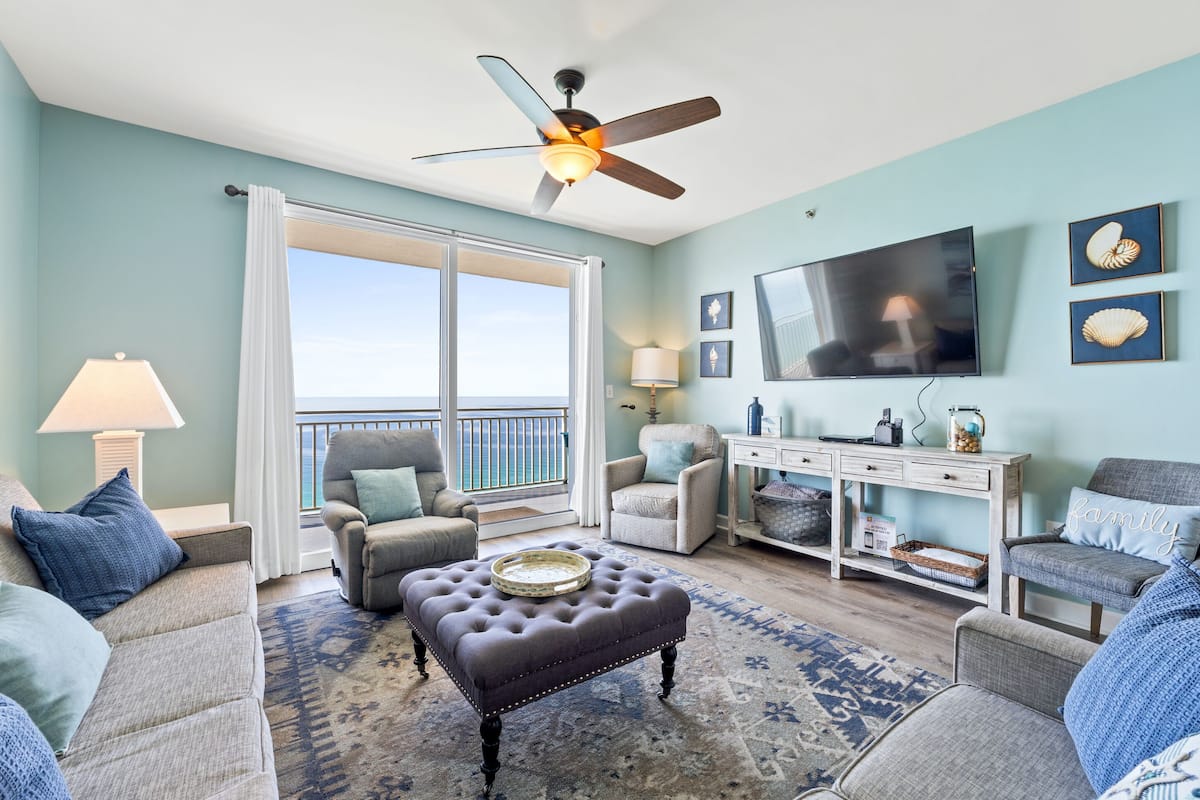 A living room with a large window, a ceiling fan, a flat-screen TV, and a console table with decorative items.
