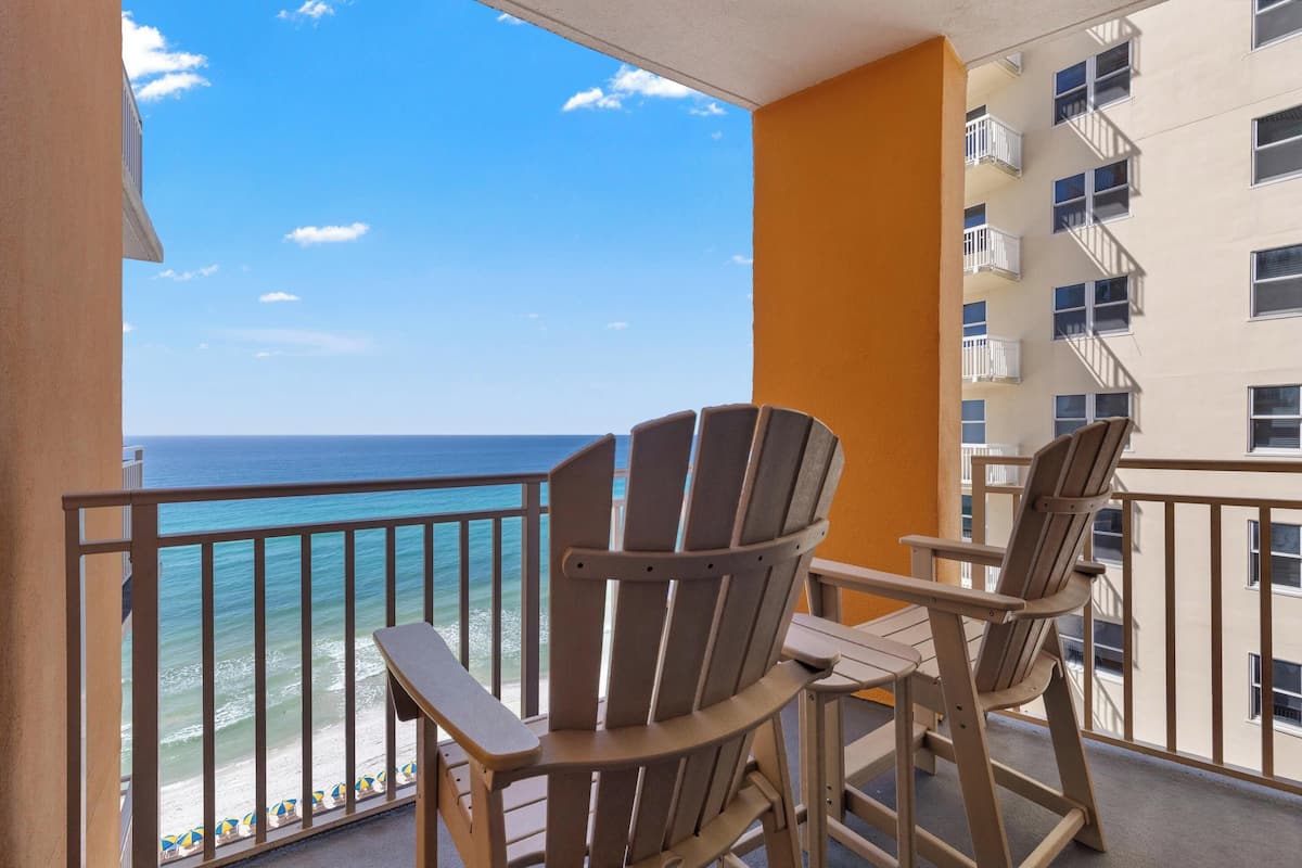 A balcony with two Adirondack chairs, a view of the ocean, and a building with balconies.