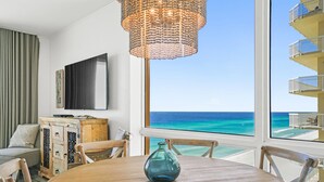 A room with a wooden dining table, a blue vase, a wicker chandelier, a flat-screen TV, and a view of the ocean. - Splash Beach Resort by Panhandle Getaways (Panama City Beach)