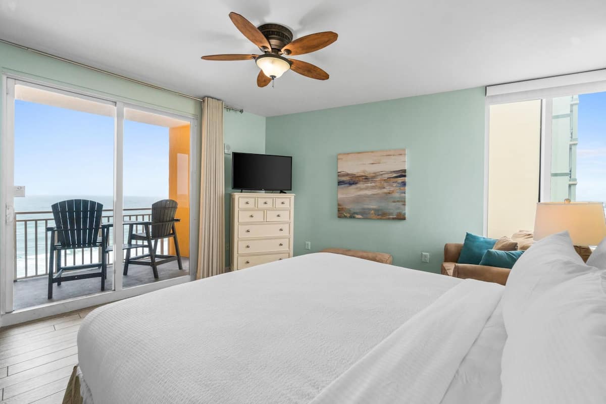 A bedroom with a large bed, a ceiling fan, a TV, a dresser, and a painting.
