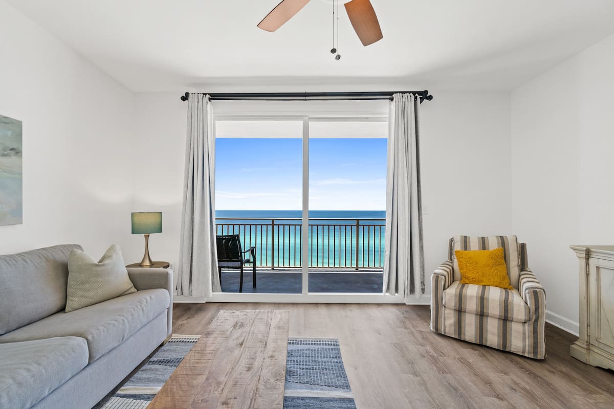 A living room with a sofa, armchair, and a view of the ocean through a sliding door.
