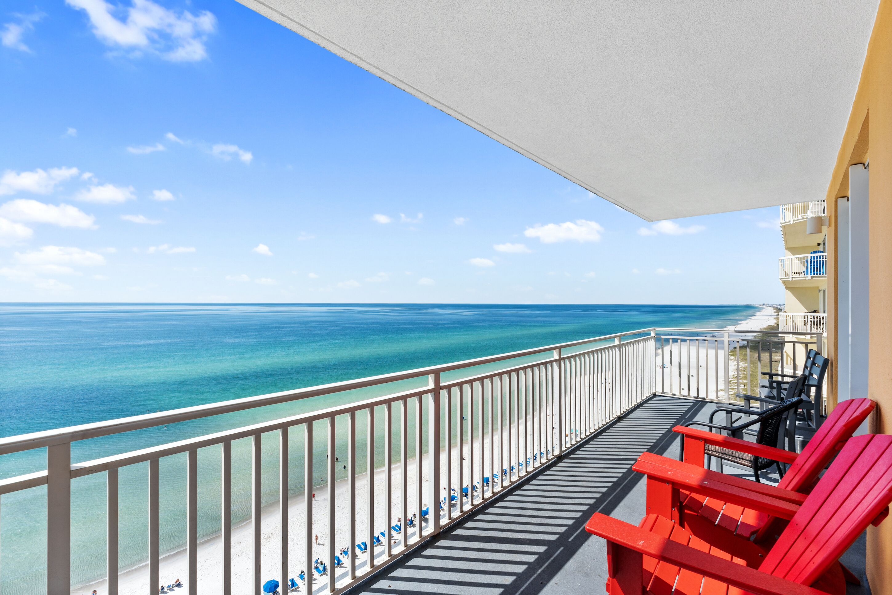 A balcony with a view of the ocean, a beach, and a building with balconies.