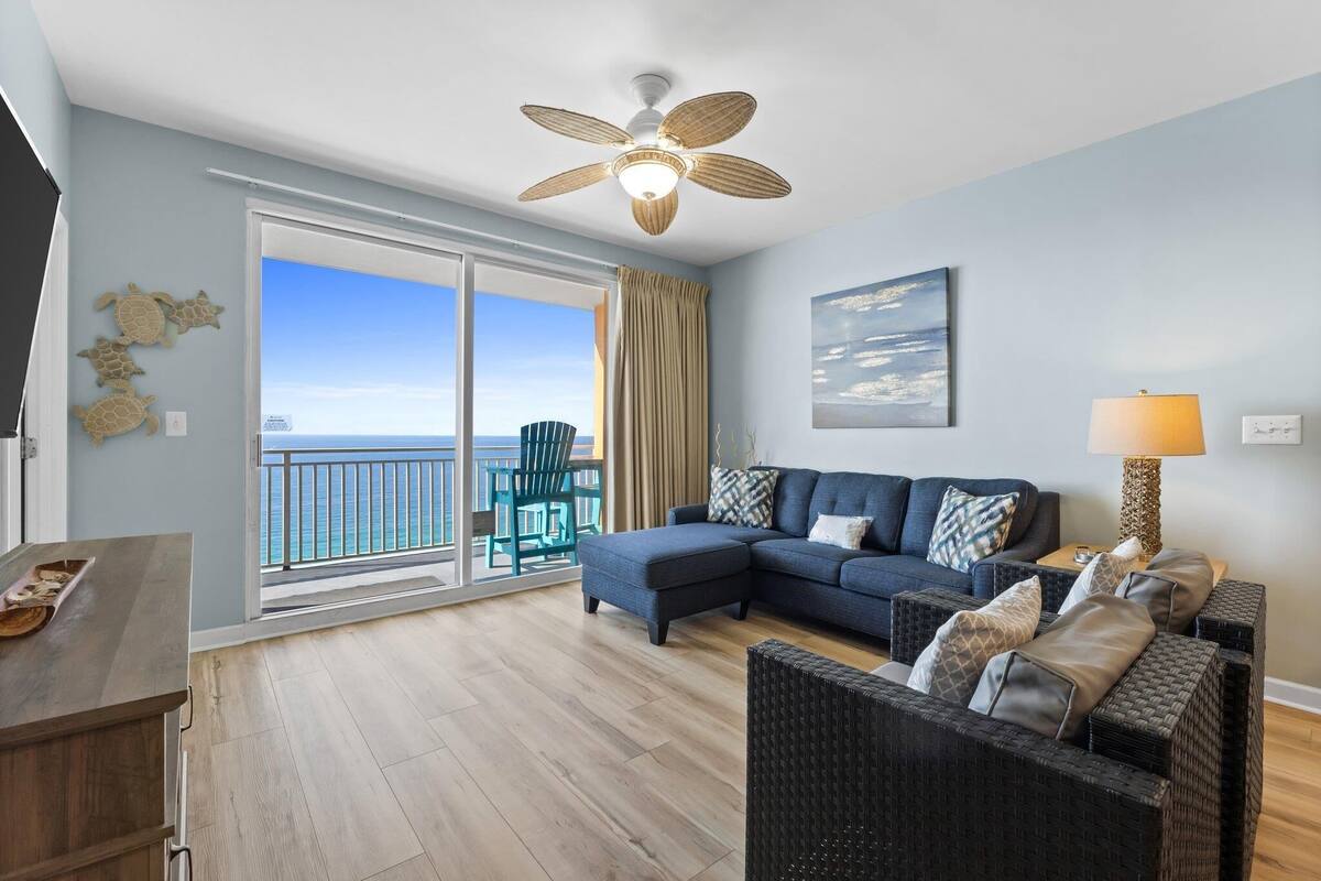 A living room with a large window, a ceiling fan, a sofa, a coffee table, and a lamp.