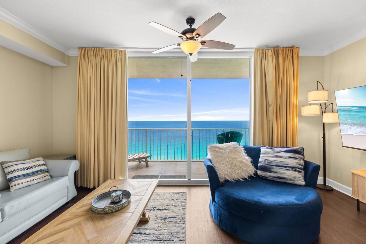 Une chambre avec un balcon, un ventilateur de plafond, un canapé, un fauteuil et une télévision.