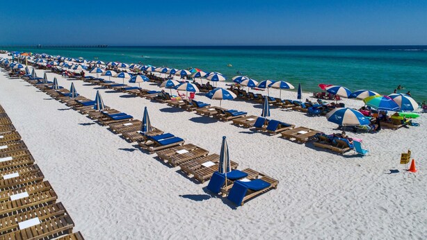 Une plage bordée de rangées de chaises longues et de parasols, un ciel bleu azur et l’océan en toile de fond.