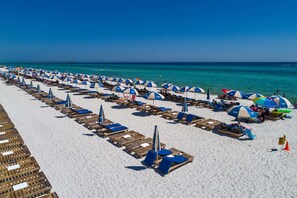 En strand med rækker af liggestole og parasoller, en klar blå himmel og havet i baggrunden.