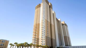 A tall, modern hotel with multiple floors and balconies, surrounded by palm trees.