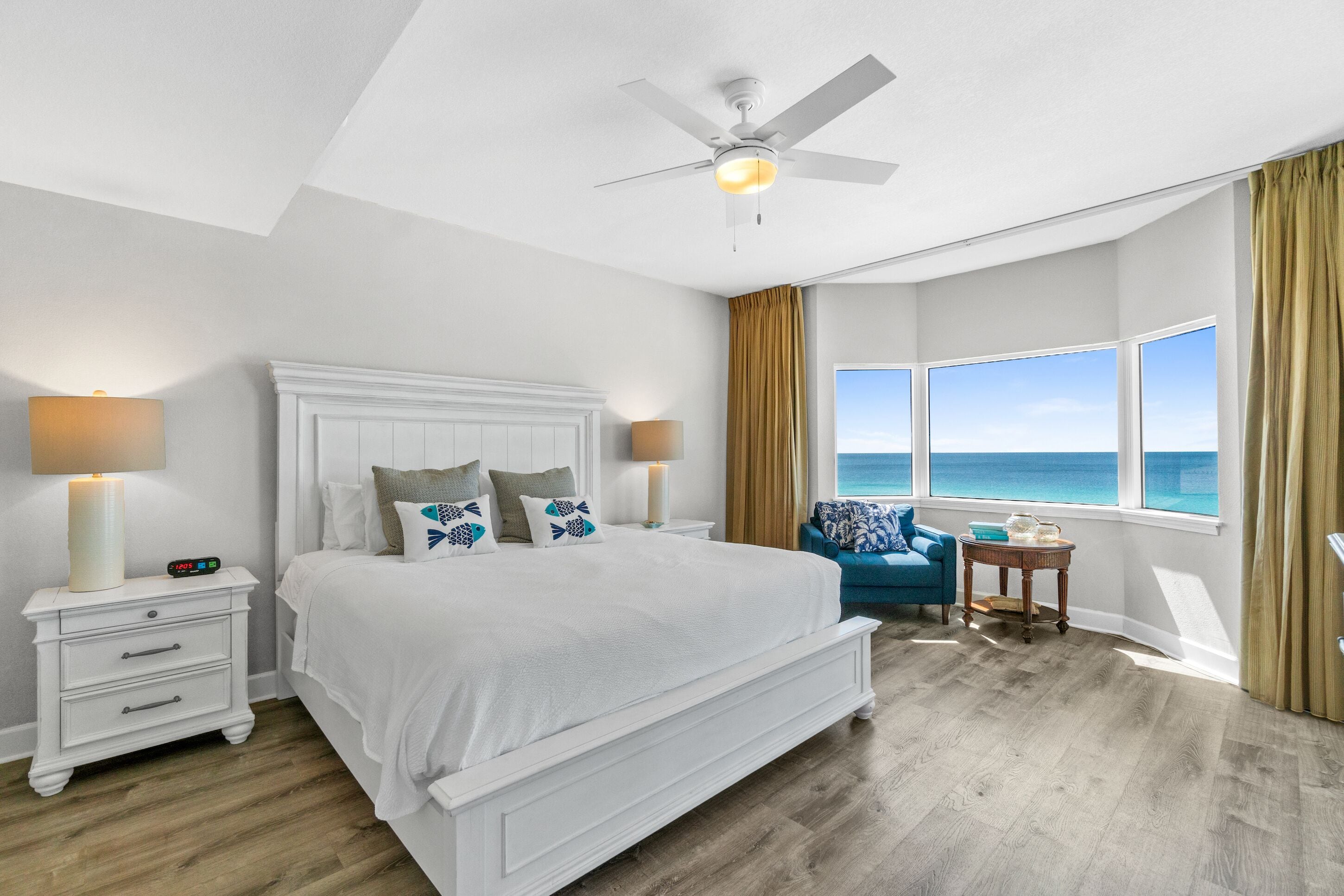 A bedroom with a large bed, a nightstand, a table, and a view of the ocean.