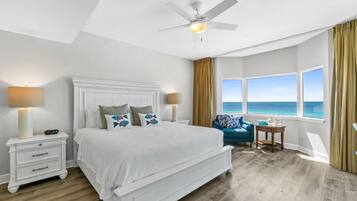 A bedroom with a large bed, a nightstand, a table, and a view of the ocean.