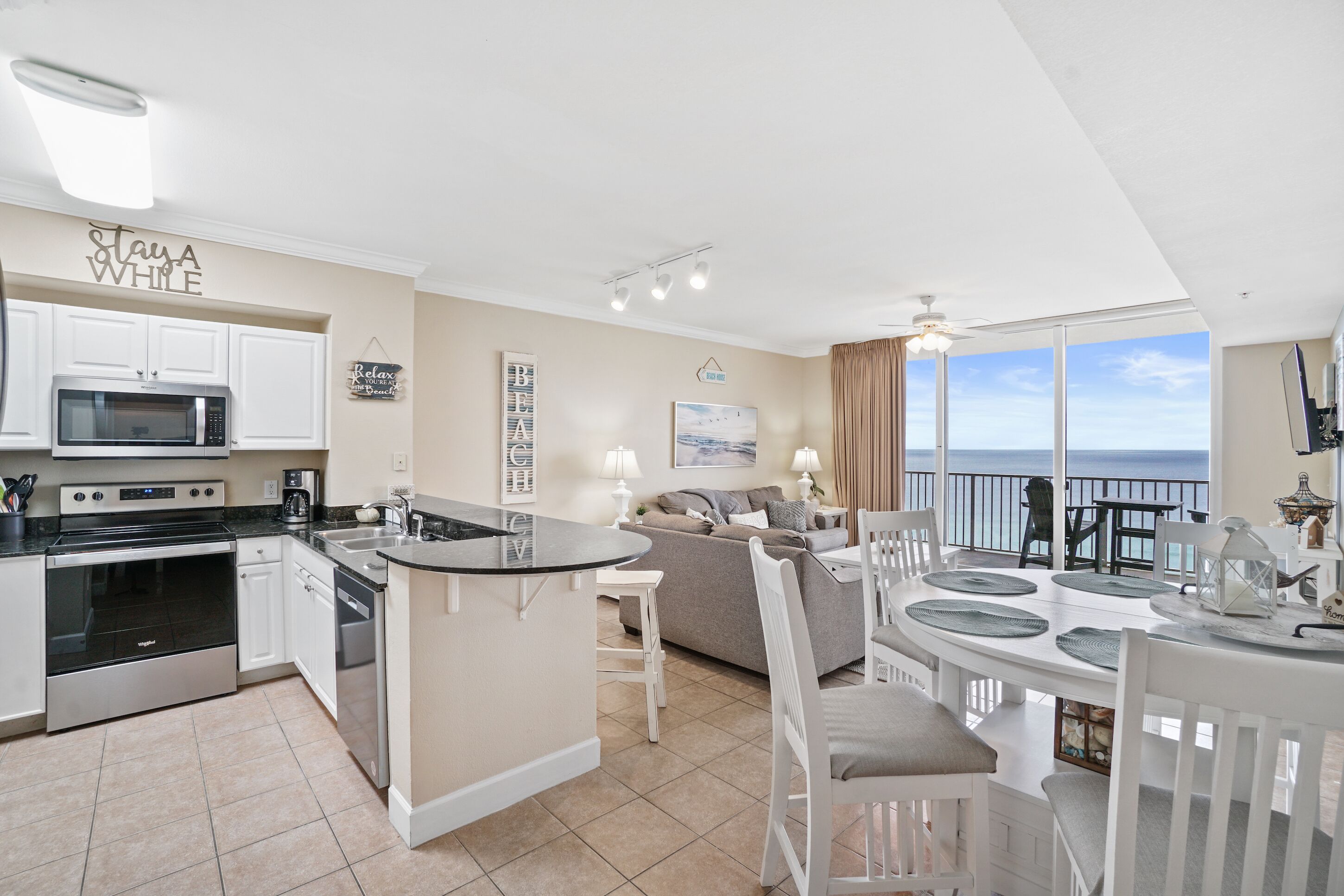 A modern kitchen with a central island, white cabinetry, and a large window overlooking the ocean.