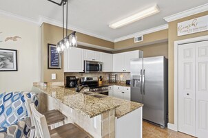 A kitchen with white cabinets, a stainless steel refrigerator, a microwave, and a granite countertop.