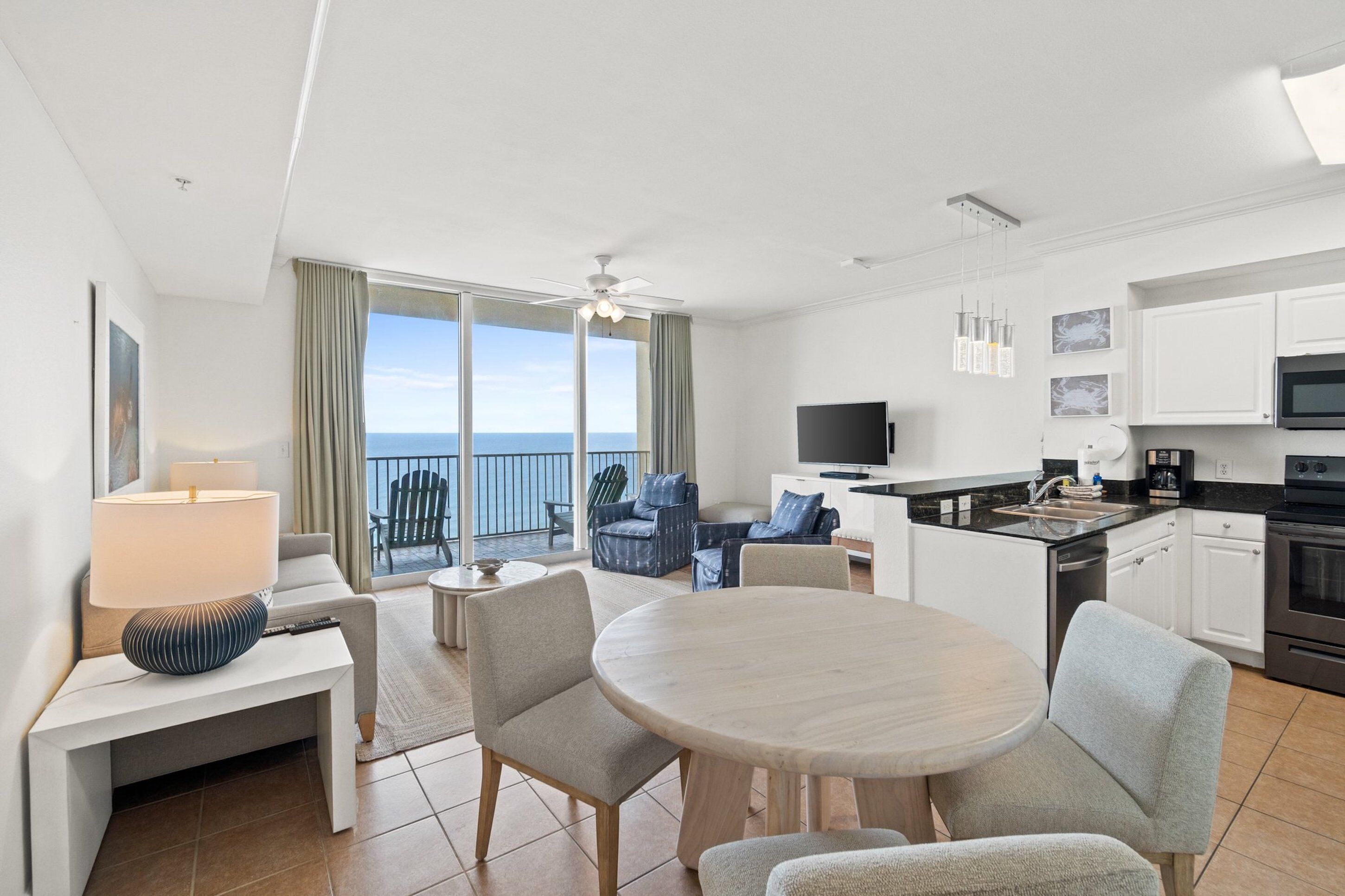 Una habitación de hotel moderna con balcón, zona de comedor, cocina y televisor.