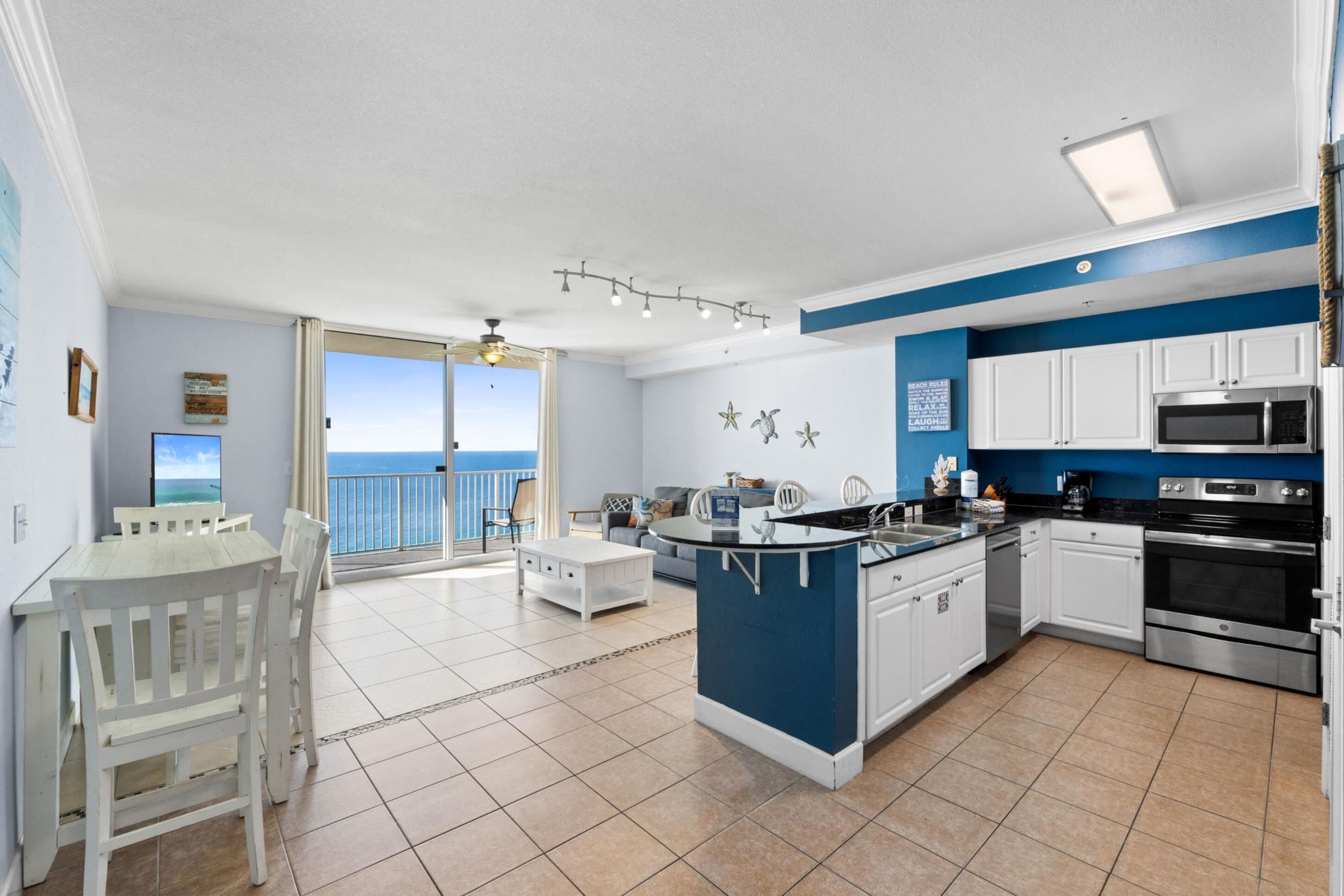 A modern kitchen with white cabinets, a central island, and a view of the ocean through the sliding glass door.