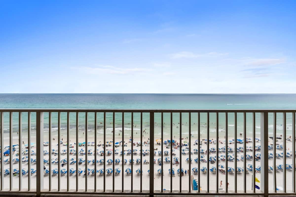 Une plage bordée de rangées de parasols et de chaises longues, un ciel dégagé et l’océan en toile de fond.