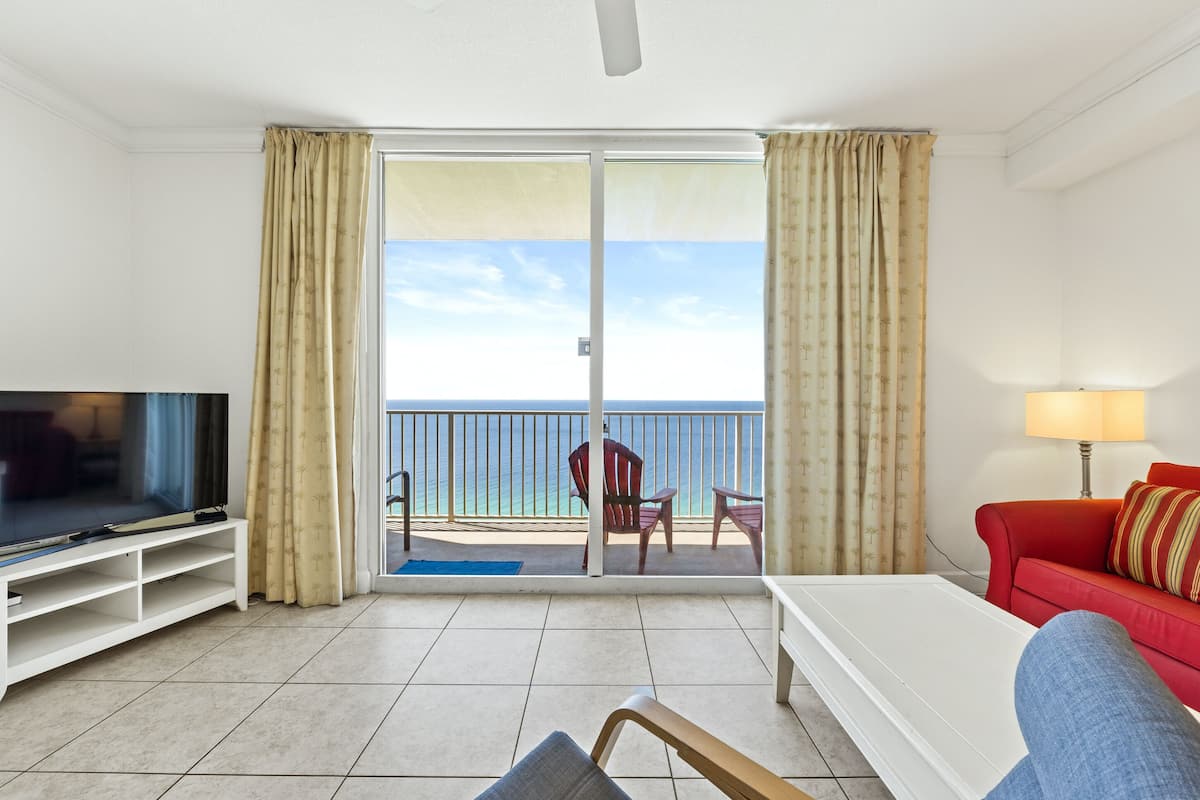Un salon équipé d’un téléviseur, d’un canapé rouge, d’une table basse blanche et d’un balcon offrant une vue sur la mer.