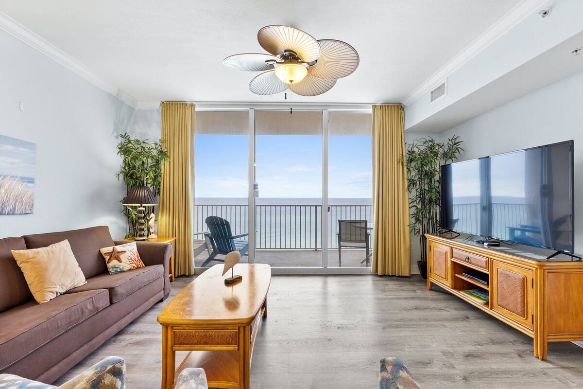 Un salon moderne avec un canapé, une table basse, un téléviseur et un balcon agrémenté de rideaux.