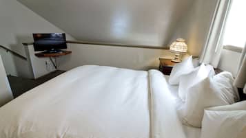 A hotel room with a bed, a television on a stand, a nightstand with a lamp, and a window with curtains.