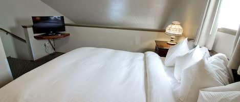 A hotel room with a bed, a television on a stand, a nightstand with a lamp, and a window with curtains.