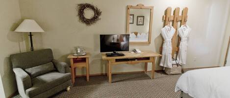 A hotel room with a sofa, a desk with a TV, a mirror, and a bed.