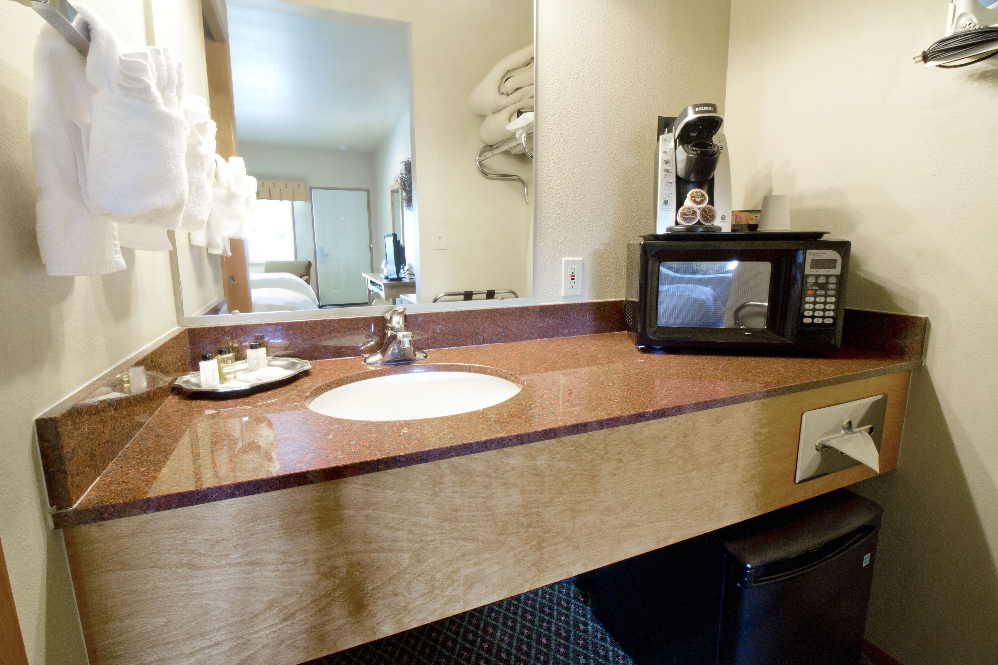 A bathroom with a sink, a mirror, a towel rack, a coffee maker, and a trash bin.
